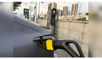 理想超充黑色充電槍透過黃色 v.NEXT-mini 轉接頭連接車輛，後方為理想充電樁